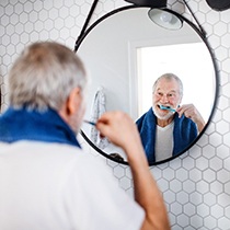 Senior man brushing his teeth in front of bathroom mirror